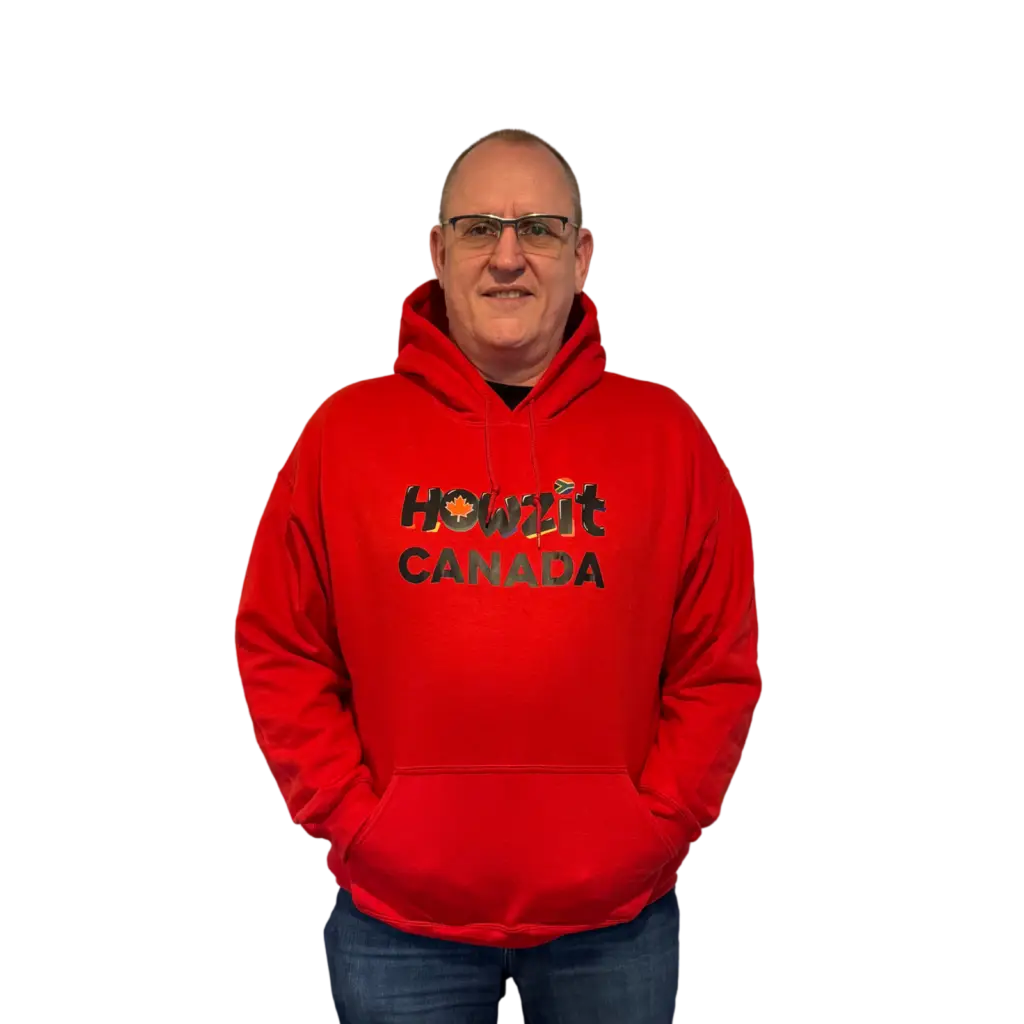Man wearing a red Howzit Canada hoodie, smiling and standing with hands in pockets.