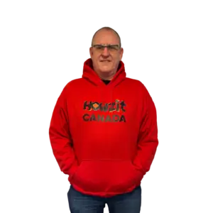 Man wearing a red Howzit Canada hoodie, smiling and standing with hands in pockets.