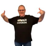 Man wearing a black Howzit Canada T-shirt, pointing to the logo on the front with a big smile.