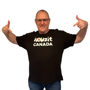 Man wearing a black Howzit Canada T-shirt, pointing to the logo on the front with a big smile.
