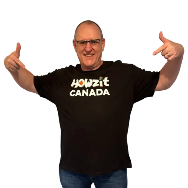 Man wearing a black Howzit Canada T-shirt, pointing to the logo on the front with a big smile.