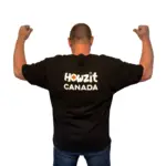 Man wearing a black Howzit Canada T-shirt, flexing his arms, showcasing the South African-Canadian themed design.