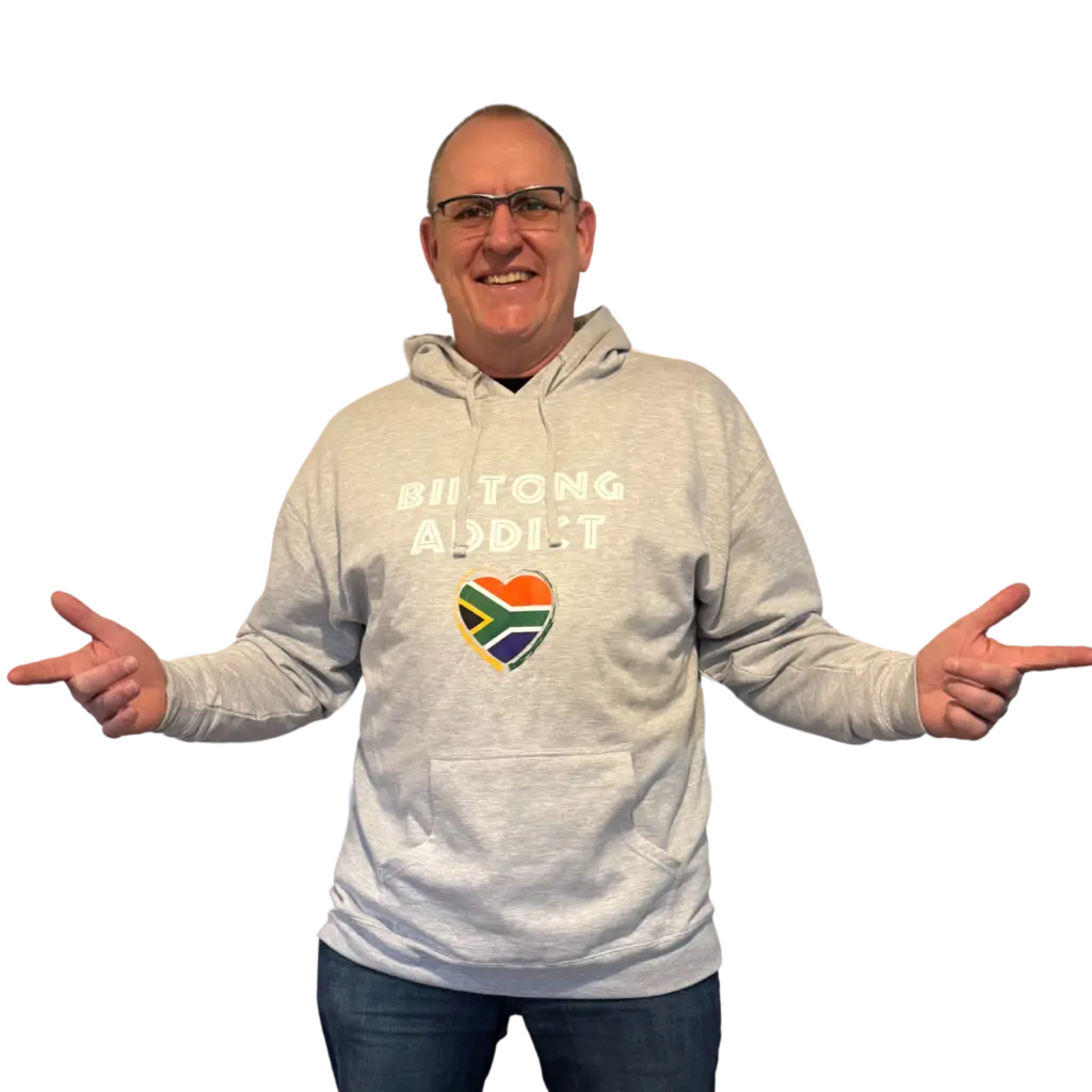Man wearing a gray Biltong Addict hoodie, smiling and pointing at the design featuring bold text and a South African flag heart.