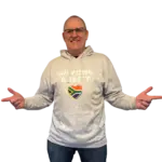 Man wearing a gray Biltong Addict hoodie, smiling and pointing at the design featuring bold text and a South African flag heart.